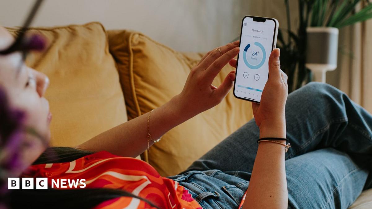 A picture of a woman in a red t shirt and jeans leaned back on a sofa checking her energy consumption on a mobile app.